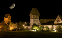 Mittelalterliche Fachwerkhäuser bei Nacht mit halbmondbeleuchtetem Himmel.