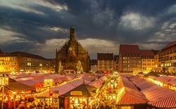 Abendlicher Weihnachtsmarkt mit beleuchteten Ständen und gotischer Kirche im Hintergrund.