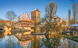 Fachwerkhaus und Brücke an einem Fluss im Winter, mit blauem Himmel im Hintergrund.