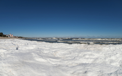 Winterliche Strandlandschaft mit Schnee und Meer im Hintergrund.