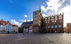 Marktplatz mit historischem Gebäude und Weihnachtsbaum bei klarem Himmel.
