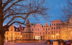 Historischer Marktplatz mit Brunnen und beleuchteten Gebäuden bei Abenddämmerung.