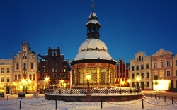 Winterliche Wasserkunst und historische Gebäude bei Nacht, verschneit.