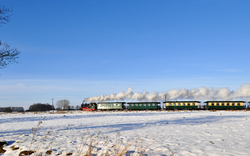 Dampfzug fährt durch verschneite Landschaft unter blauem Himmel
