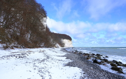 Verschneiter Strand mit Klippen und Meer unter blauem Himmel