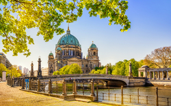 Berliner Dom im Sommer bei sonnigem Wetter, an der Spree gelegen, umgeben von grünen Bäumen.