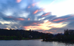 Sonnenuntergang über See mit bewölktem Himmel und Bäumen im Hintergrund