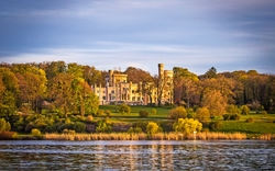 Schloss am Seeufer, umgeben von Bäumen im Sonnenuntergang.