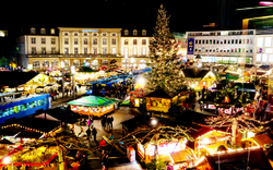 Nachtansicht des Kasseler Märchen-Weihnachtsmarkts mit geschmücktem Tannenbaum.