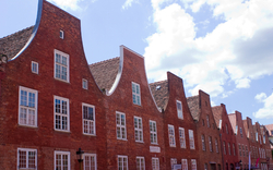 Rote Backsteinhäuser mit geschwungenen Giebeln und vielen Fenstern unter blauem Himmel.