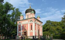 Rosa orthodoxe Kirche mit Zwiebeltürmen im Grünen unter blauem Himmel.
