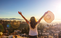 Frau steht mit Hut in der Hand vor Stadtpanorama bei Sonnenuntergang.