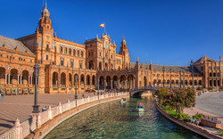 Plaza de España in Sevilla bei sonnigem Wetter mit Wasserkanal und Booten im Vordergrund.