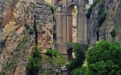 Alte Steinbrücke über tiefe Schlucht mit Wasserfall und Vegetation.