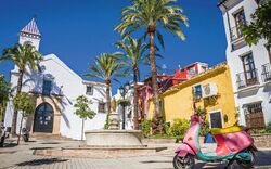Bunter Platz mit Palmen, Kirche und rosa Motorroller unter blauem Himmel