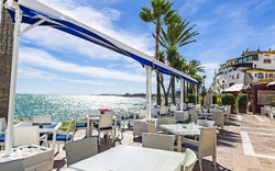 Strandpromenade mit leerem Restaurant und Blick aufs Meer bei sonnigem Wetter.