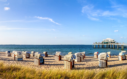 Panoramablick auf einen Strand mit Strandkörben und einer Seebrücke.