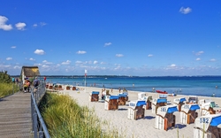 Strand mit Strandkörben, blauer Himmel und Meer im Hintergrund.