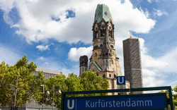 Gedächtniskirche in Berlin am Kurfürstendamm bei klarem Himmel und U-Bahn-Schild im Vordergrund.