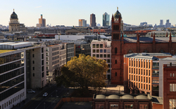 Stadtansicht mit modernen Gebäuden, Baum und Kirche bei klarem Himmel.