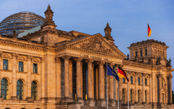 Reichstagsgebäude in Berlin bei Sonnenuntergang, mit Flaggen und Kuppel.