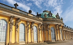 Gelbes Barockgebäude mit blauer Kuppel und verzierten Statuen unter blauem Himmel.