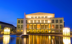 Opernhaus am Abend mit Beleuchtung und reflektierendem Wasser im Vordergrund.