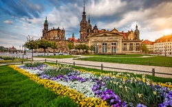 Garten mit Blumen und historische Gebäude im Hintergrund unter bewölktem Himmel.