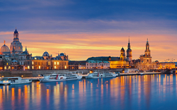 Stadtpanorama von Dresden bei Sonnenuntergang mit Elbe und beleuchteten Gebäuden.