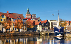 Altstadt mit Hafen, Schiff, bunten Häusern und Kirchturm im Hintergrund bei sonnigem Wetter.