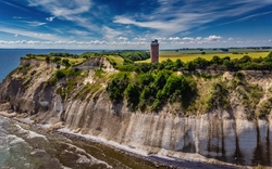 Klippenlandschaft mit Leuchtturm und bewölktem Himmel am Meer.