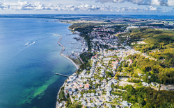Luftaufnahme einer Küstenstadt mit Hafen und bewaldetem Umland.