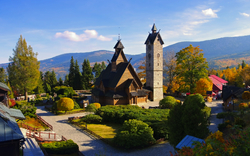 Holzkirche in herbstlicher Berglandschaft mit Turm und umliegenden Bäumen.