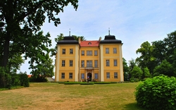 Gelbes Herrenhaus mit grüner Umgebung und klarem Himmel.