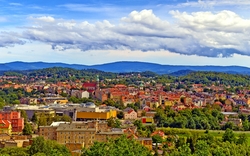 Stadtpanorama mit grünen Hügeln und bewölktem Himmel im Hintergrund.