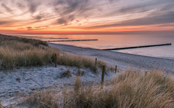 Strand bei Sonnenuntergang mit Meer, Dünen und Holzpfaden.