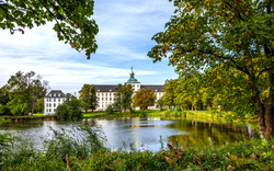 Ein Schloss am See umgeben von Bäumen und grünem Laub.