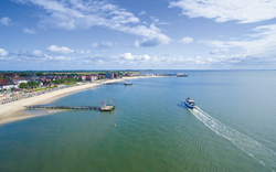 Blick auf eine Hafeneinfahrt mit einem Schiff und Strandpromenade bei sonnigem Wetter.