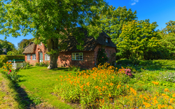 Backsteinhaus mit Reetdach in einem blühenden Garten im Sommer.
