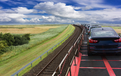 Autos auf einem Zug auf einer ländlichen Eisenbahnstrecke bei blauem Himmel