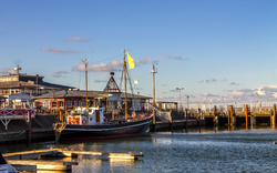 Hafen mit Booten und Gebäuden bei klarem Himmel und Sonnenschein.