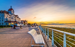 Promenade mit Bank, modernen Gebäuden und Blick auf einen Sonnenuntergang über dem Meer.