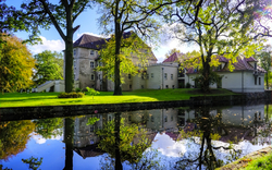 Schloss am Ufer eines Teichs mit Bäumen im Herbst.