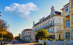 Straße mit historischen Gebäuden, Bäumen und blauem Himmel.