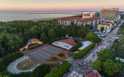 Luftaufnahme einer Promenade mit Bühne, Gebäuden und Küste bei Sonnenuntergang.