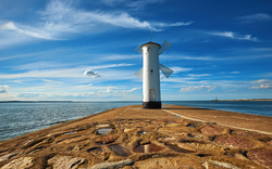 Leuchtturm auf einer Mole am Meer unter blauem Himmel.