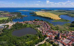Luftaufnahme einer Stadtlandschaft mit Seen und Feldern im Hintergrund.