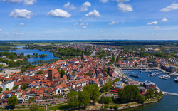 Luftaufnahme einer Stadt mit Hafen, rotem Ziegeldach und umgebender Landschaft.