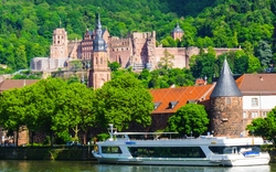 Schiff auf Fluss vor Heidelberger Schloss und grüner Hügellandschaft.