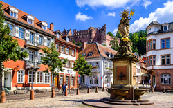 Altstadtplatz mit Springbrunnen und Schloss im Hintergrund bei sonnigem Wetter.